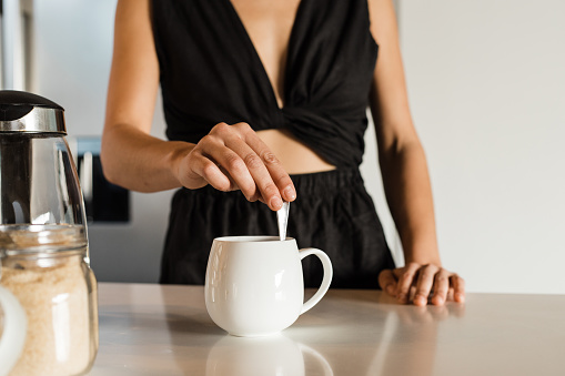 Midsection of mixed race mid adult woman wearing black attire mixing coffee in cup on kitchen island in morning