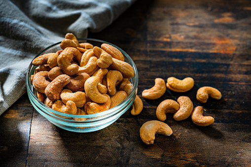 Close up view of a glass bowl filled with peanuts shot on dark rustic table.