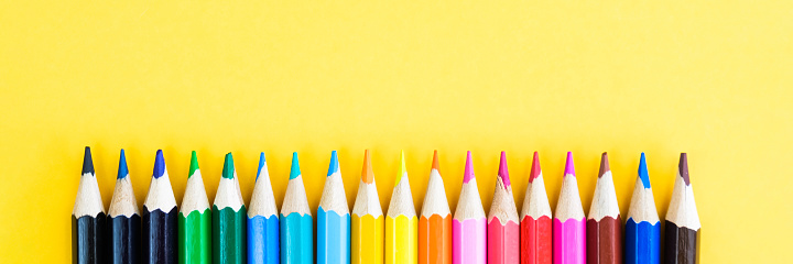 Children's multi-colored wax crayons for drawing on a white album sheet with free space for text on the right side. Left hand drawing and attention deficit hyperactivity disorder concept