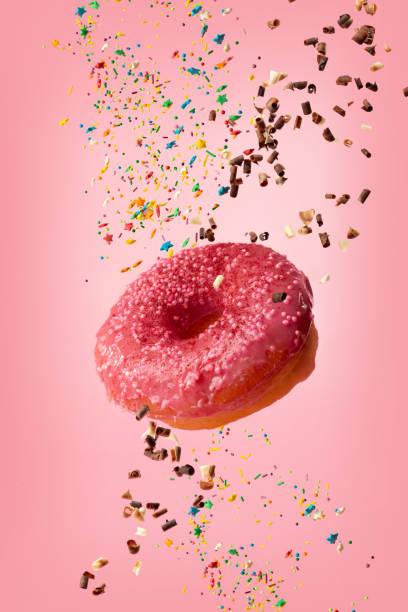 istock A glazed donut is pricked on a fork with sprinkles on a pink background . Jam is poured on a donut. 1417873477