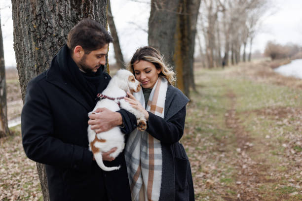Happy young couple carrying and stroking their new dog while walking in nature on cold day
