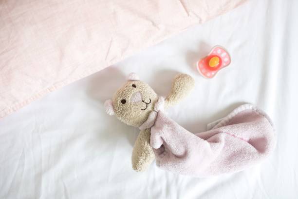 A top view of a small teddy bear and pacifier on bed