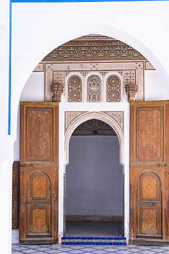 Peach colored wall with an Arch entrance decorated with traditional Moroccan mosaics and inscriptions in Arabic. Old town of Marrakech (Medina).