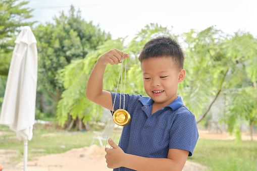 Cute little Asian school boy child having fun learning how to play with a yo-yo skill toy alone at home backyard, Soft and Selective focus