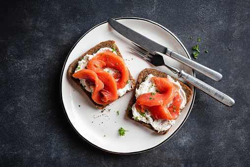 Rye bread with cream cheese and smoked salmon toast on plate, black stone background. Tasty red fish toast or open sandwich