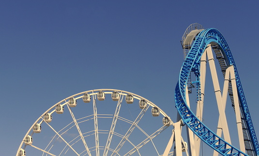 Rollercoaster and ferris wheel against blue sky in amusement park