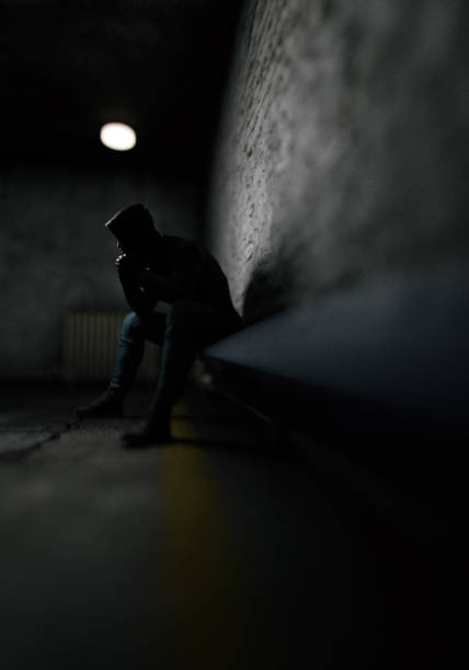 istock Man in hoodie sits on bench in dark prison. 3D render. 1417890686