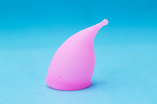 Pink female vaginal menstrual cup on a blue background, close-up. Medical silicone bowl for girls for collecting discharge during menstruation