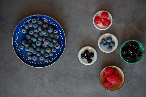 Blackberries, raspberries and blueberries in small bowls on a table - from above