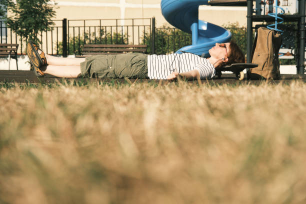 Active mid adult woman is relaxing on sunny sportsground holding her head on the skateboard