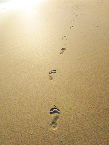 Footprints on a sandy beach with sun behind, Sabang, Palawan, Philippines.
