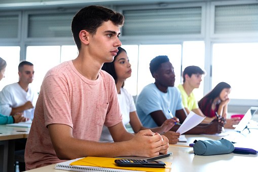 Caucasian teen male high school student in class listening to teacher. Multiracial university students in classroom listen to lecture. Copy space. Education concept.