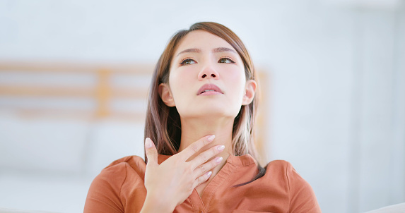 portrait of asian woman coughing feeling uncomfortable in winter at home - she touches her throat
