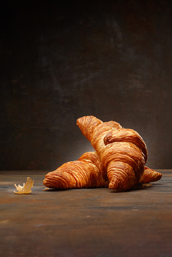 French pastry. Two fresh croissants on dark brown mood background, copy space for your product. Close up of pile of delicious croissants on a dark rusty background. Selective focus.