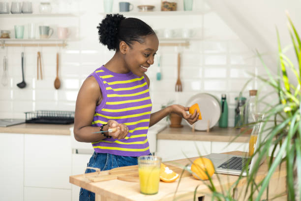 istock African young woman making orange juice and using laptop 1417899138