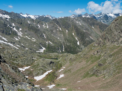 view of mountain valley with winding stream of spring and snow-capped peaks at Stubai hiking trail, Stubai Hohenweg, Summer rocky alpine landscape of Tyrol, Stubai Alps, Austria.