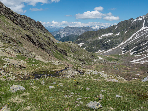 view of mountain valley with winding stream of spring and snow-capped peaks at Stubai hiking trail, Stubai Hohenweg, Summer rocky alpine landscape of Tyrol, Stubai Alps, Austria.