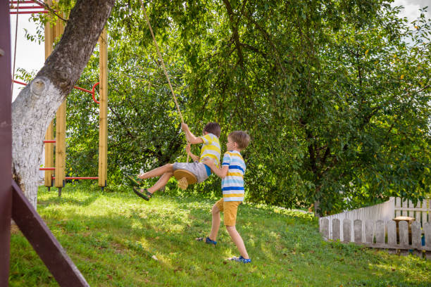 istock Two adorable happy little boys is having fun on a rope swing which he has found while having rest outside city. Active leisure time with children 1417906825