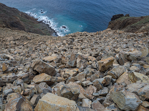 steep slope of rock falling stones with lava cliffs and blue sea background