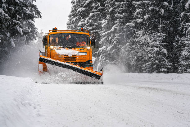 Orange maintenance plough truck on forest road after snowstorm blizzard. Roads get dangerous during winter (driver face blurred) stock photo