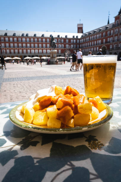 una porzione di tapas in plaza mayor a madrid. patate con salsa alioli e salsa brava con una birra. - piazza delle vettovaglie foto e immagini stock