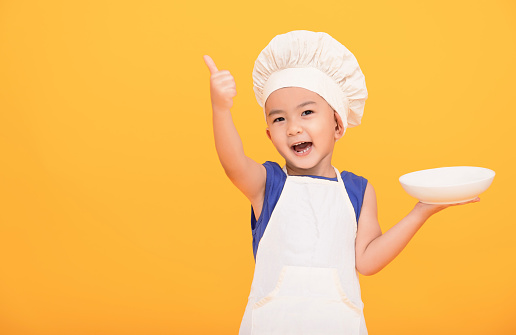 Happy boy in chef uniform showing thumbs up on yellow background