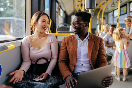 A young black man is talking to an Asian woman on the city bus