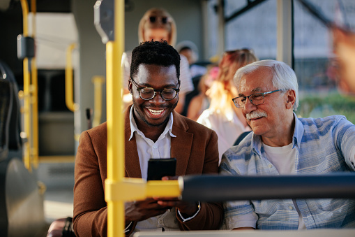 Black man is showing a caucasian senior man his smartphone on the public transport