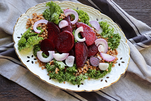 Warm buckwheat and beetroot salad on wooden background. Vegetarian diet idea and recipe -salad with beetroot, buckwheat, kale, onion, fresh herbs. Top view or flat-lay .