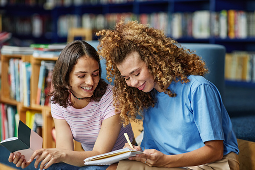 Vibrant portrait of two young girls studying in college library and smiling happily