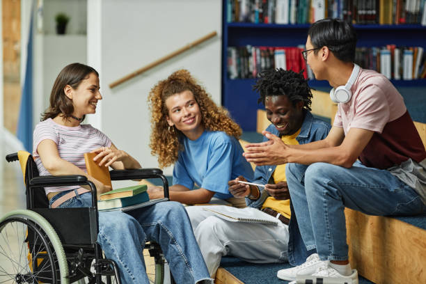 Diverse Group of Students Chatting Diverse group of young people chatting in college library including female student with disability education stage stock pictures, royalty-free photos & images