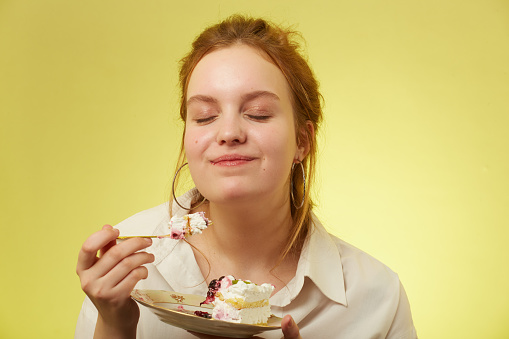 fun pretty red hair girl with down syndrome eats sweet dessert on yellow background