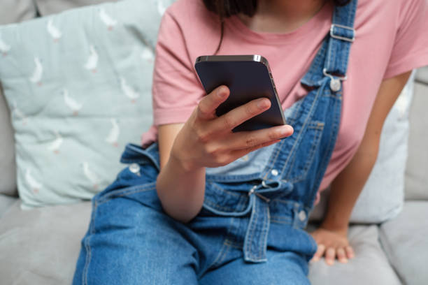 istock Cropped Image Of Woman with Bib Overalls using phone on coach 1417932399