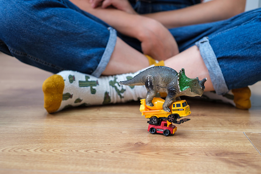 Girl on wooden floor playing with cars and dinosaurs toys.