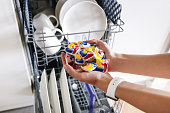 Dishwashing capsules. Open dishwasher with clean dishes in a white kitchen. Dishwasher Detergents in hands.dishwasher gel capsules. Capsule for the dishwasher. Brilliant cleanliness.