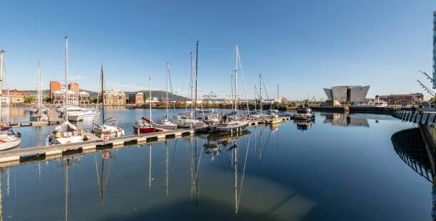 Belfast, UK. 12 August 2022. Boats in Belfast harbour with various buildings and people walking around.