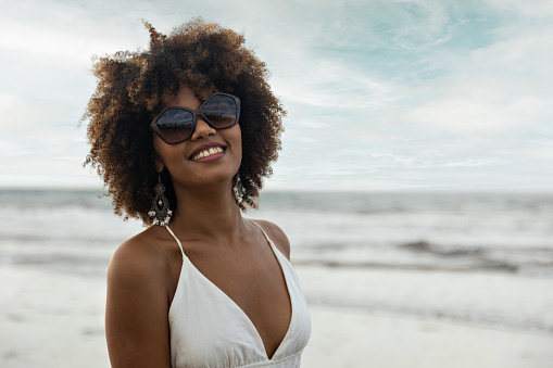 Portrait of beautiful smiling black woman with curly hair wearing sunglasses on the beach.