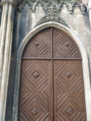 Amazing big old arched two-leaf wooden door under a semicircular arch of stone. Brown door with a ornate gothic elements.