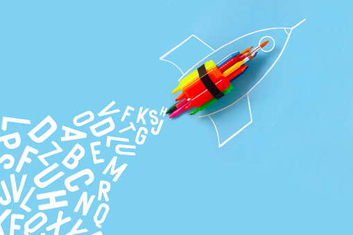 Rocket ship made by crayons and school supplies on blue background with letters