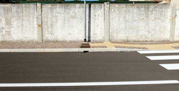 istock Grunge concrete wall with a pole in the middle, on the sidewalk. Asphalt road in front. 1417945832