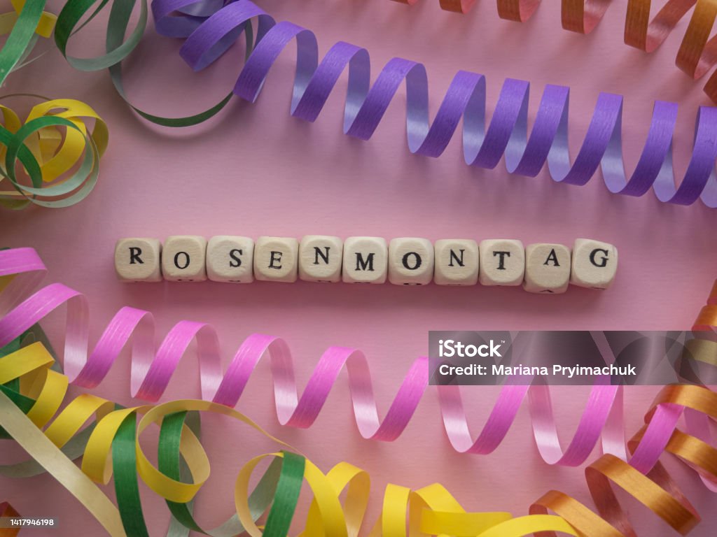 Rosenmontag in wooden cubes on pink background German text Rosenmontag, translate Carnival Monday. Rosenmontag in wooden cubes on pink background with coiled streamers. Carnival in Germany. Carnival - Celebration Event Stock Photo