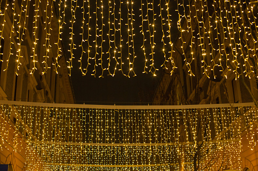 Christmas decor with lights on the street. Vibrant gold night illumination of New Year holiday. Glowing festive New Year decoration. Atmospheric festive street.
