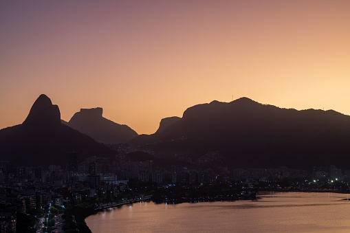 A scenic view of a silhouette of mountains and modern buildings by coast in Rio de Janeiro at sunset