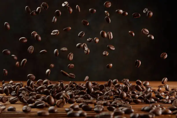 Many roasted coffee beans flying in the air. Falling coffee beans on a background of dark wall and wooden table. Shallow depth of field