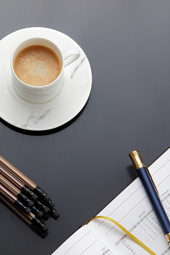 Still life, business, planning or working concept: coffee сup, calendar, diary, pen on gray desk table, top view. Copy space