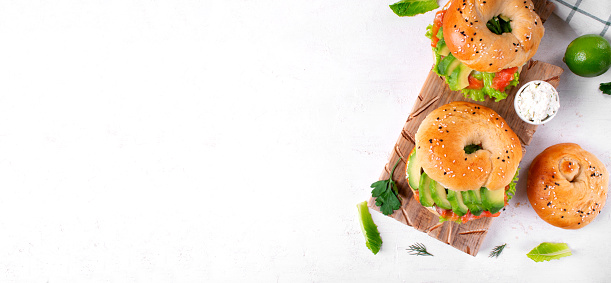 Web banner with bagel sandwich with avocado, salted trout, lettuce and cream cheese on wooden board. Top view. Mockup with copy space on white