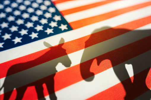 Democrats vs republicans are in a ideological duel on the american flag. In American politics US parties are represented by either the democrat donkey or republican elephant. animal shadows on flag
