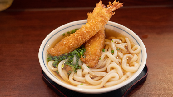 Top view, close-up of a bowl of tempura prawn udon, fried shimp and clear soup japanese noodkes served with sliced spring onion. Asian food concept.