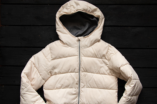 women's puffy light winter jacket lies on a black wooden table, women's winter clothes on the table flat lay