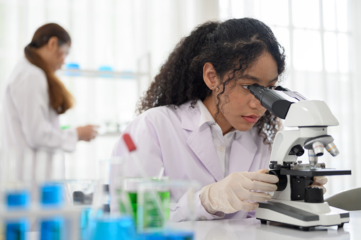 Young scientist looking in microscope while working on medical research in science laboratory.